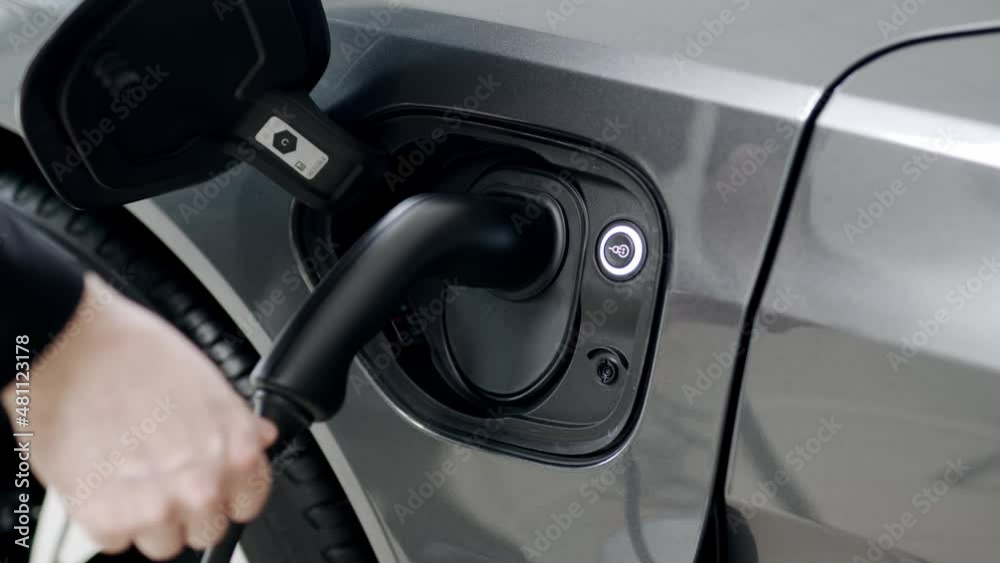 Woman hand inserts power connector into EV car. Unrecognizable person plugging in charging cable to to electric vehicle and charges batteries. Electric vehicle charging technology concept 4K Woman hand inserts power connector into EV car. Unrecognizable person plugging in charging cable to to electric vehicle and charges batteries. Electric vehicle charging technology concept 4K