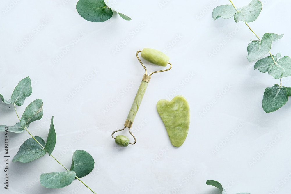 Jade stone facial roller and gua sha on stone table with green eucalyptus  leaves. Face skin care concept. Flat lay, top view. Stock Photo | Adobe  Stock