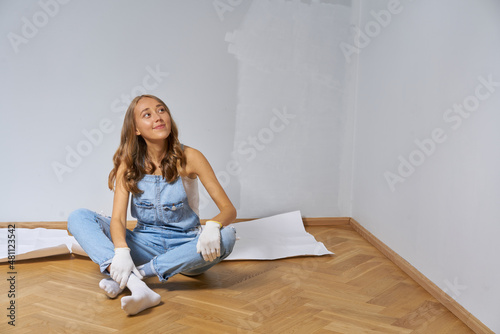 Young cute woman renovate and paint white color wall. Girl in blue denim overall happy to work