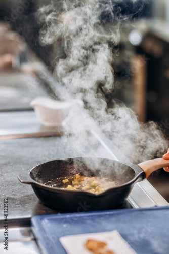 White smoke from a frying pan on a stove in a restaurant kitchen