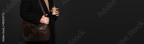 partial view of man in coat standing with paper cup and leather bag isolated on black, banner.