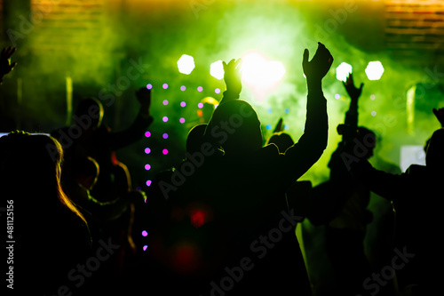 cheering crowd in front of bright yellow green stage lights. Silhouette image of people dance in disco night club or concert at a music festival.