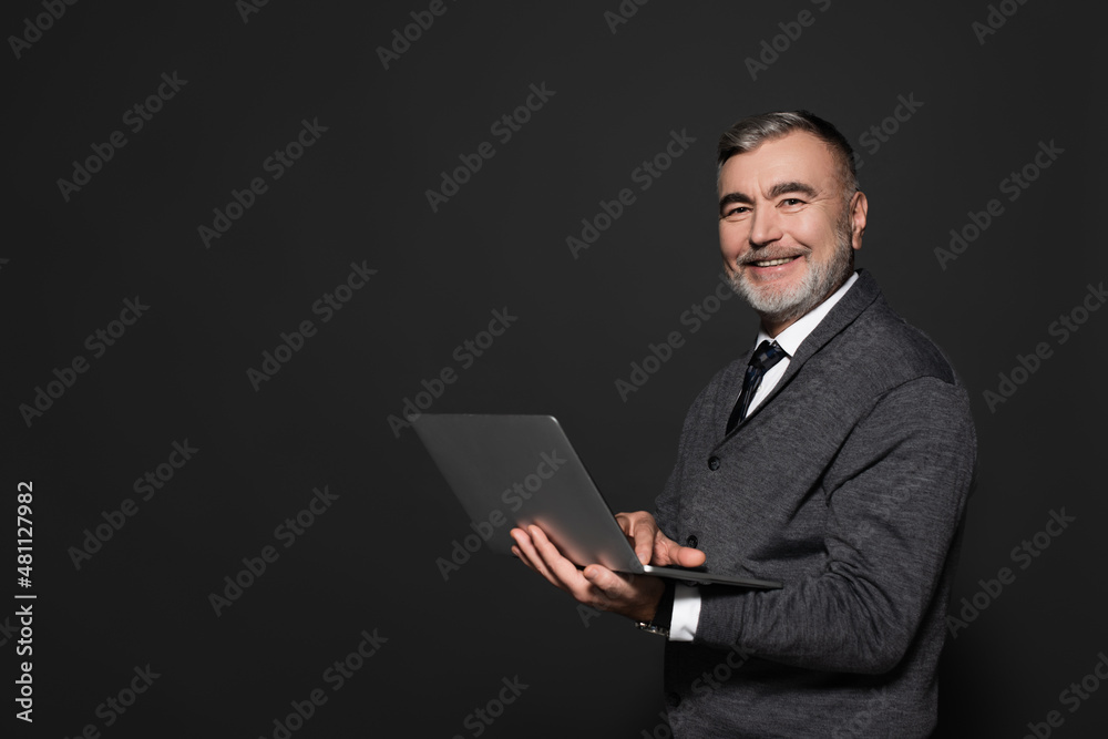 happy senior man with laptop looking at camera isolated on dark grey. happy senior man with laptop looking at camera isolated on dark grey.