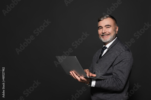 happy senior man with laptop looking at camera isolated on dark grey.