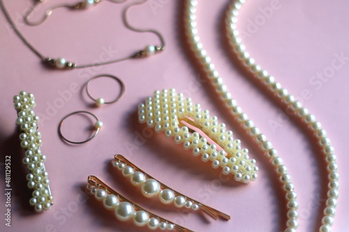Various pearl jewelry and hair accessories on pink background. Selective focus.