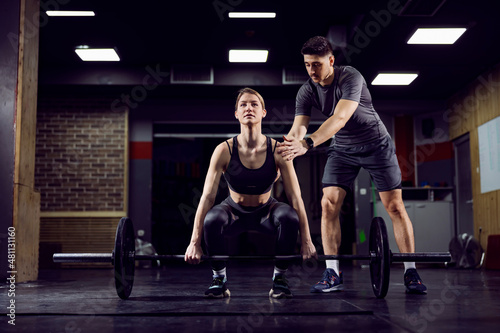 A young strong sportswoman lifting weights in gym with her personal trainer.