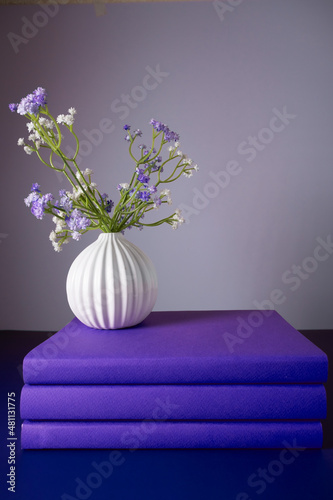 Three books in a purple cover stand on a purple background with a vase of flowers photo