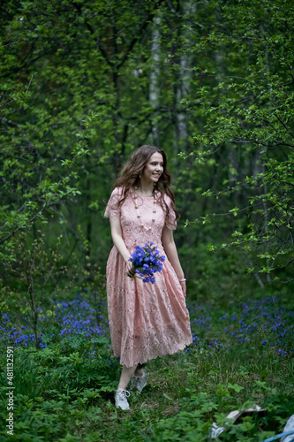 A young girl walks in a field of blue flowers at dusk.