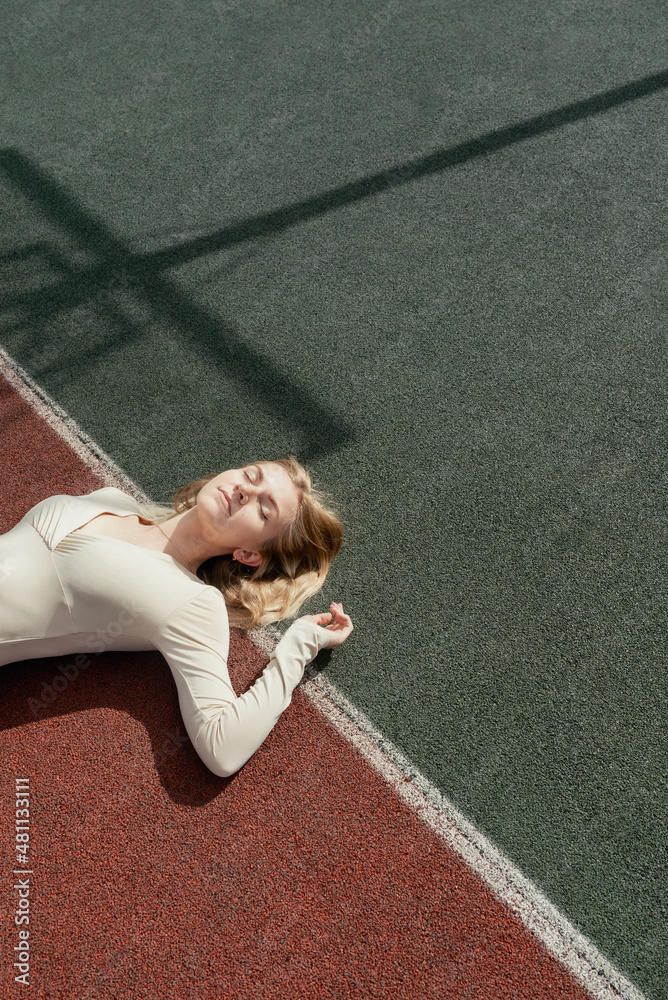 Young blonde female lying on a backetball sport field wih her eyes closed