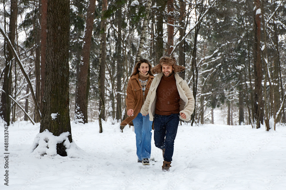 People, season, love and leisure concept - happy couple hugging and laughing outdoors in winter. Couple embracing and having fun in snowy winter park