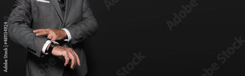 cropped view of man in suit checking time on wristwatch isolated on dark grey, banner.