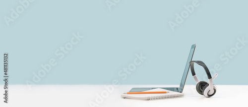 Side view of slim laptop with headphones headset on white desk. Mockup screen. Distant learning. working from home, online courses or support. Audio podcast. Helpdesk or call center banner