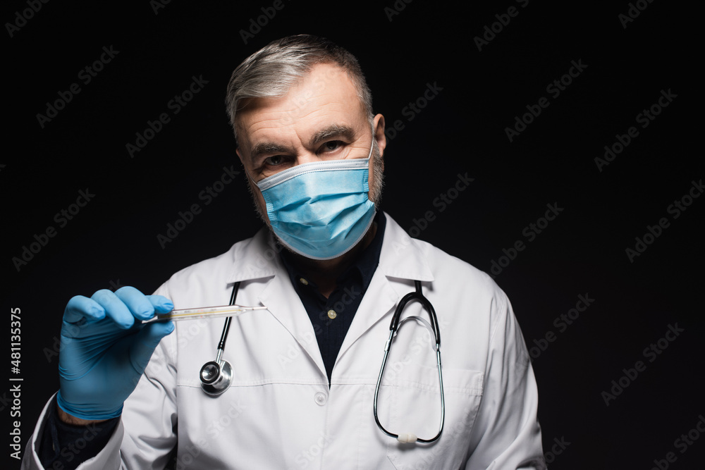 doctor in medical mask and white coat holding thermometer isolated on black. doctor in medical mask and white coat holding thermometer isolated on black.