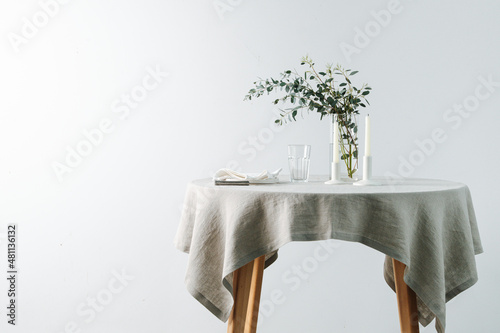 Round table with a white tablecloth decorated with candles and decorative branch. Over a white wall. photo