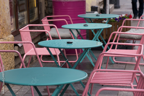 colorful turquoise blue tables and pink chairs of an empty restaurant café terrace outside on the street of a city