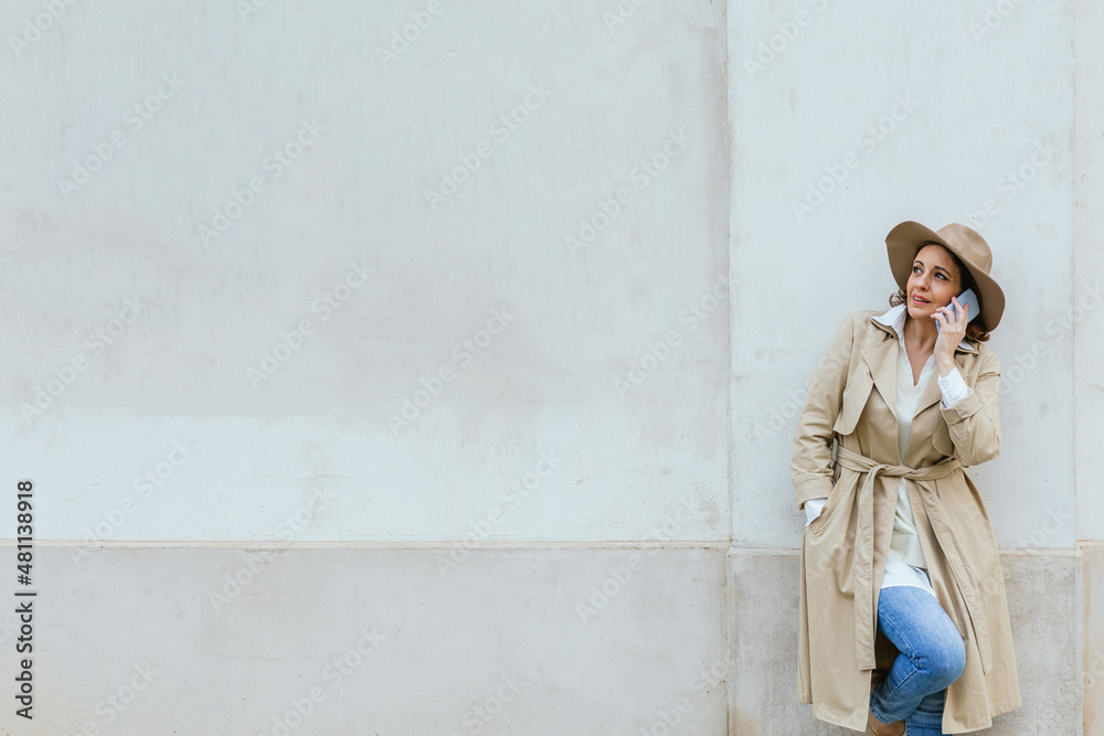 Obraz premium Woman in stylish warm clothes talking on the phone while standing outdoors on the street.