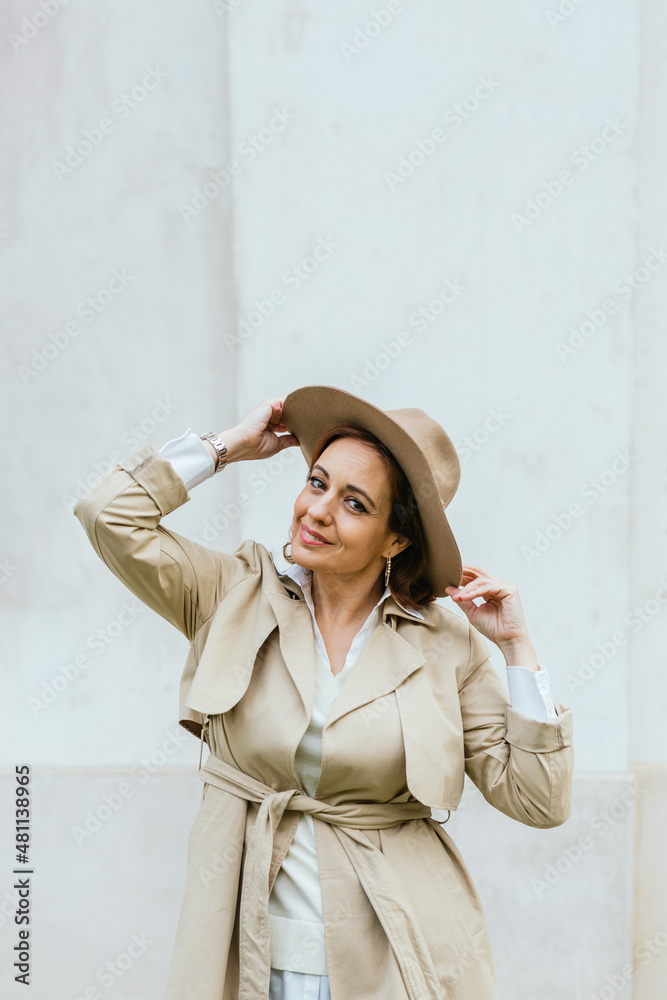 Woman in stylish trench coat and hat looking at camera while posing outdoors on the street. Woman in stylish trench coat and hat looking at camera while posing outdoors on the street.