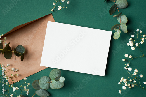 Invitation or greeting card mockup with envelope, eucalyptus and gypsophila flowers on paper background