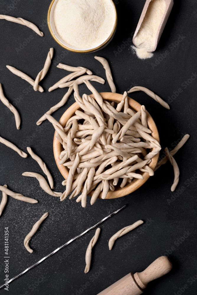 Whole grain wheat raw apulian pasta called Pizzarieddi or maccaruni in a bowl on black table. Fresh maccheroni typical dish of Puglia, Salento Italy. Italian homemade pasta background, top view, above