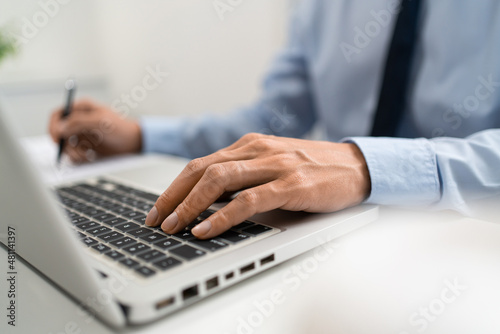 Working Man Conept The male officer sitting in the office  laying his left hand on the laptop  and writing something on the paper with his right hand