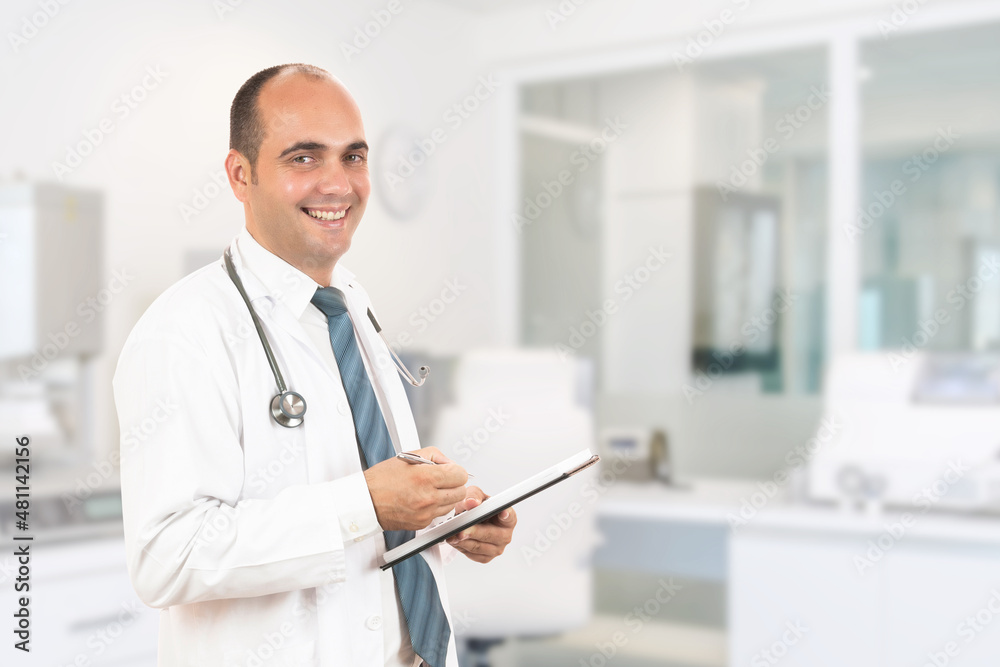 Male doctor with stethoscope holding a notebook. Smiling male doctor filling out medical form on clipboard while standing straight in hospital