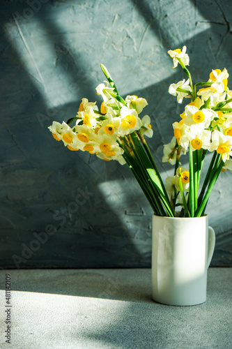 Bunch of narcissus flowers in a vase casting shadows on a table photo