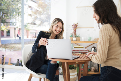 Two women have a business meeting inside a coworking space. One of them smiles and shows her something on the laptop.