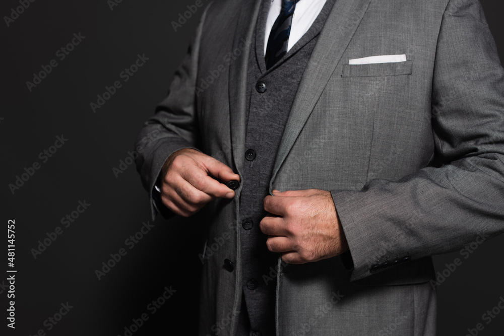cropped view of businessman buttoning blazer on dark grey background.