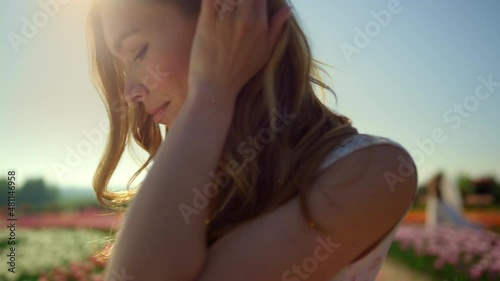 Portrait of beautiful woman arranging hair in sunlight. Relaxed female in garden