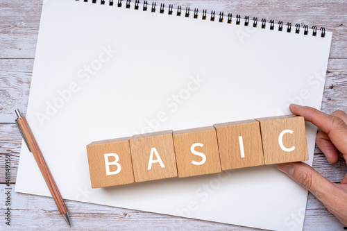 「BASIC」と書かれた積み木とペン、ノート、人の手 photo