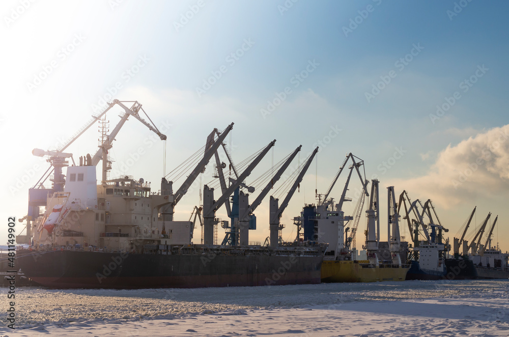 Shipyards on the bay in winter. Cranes, trawlers and ships at sunset on a frosty day.