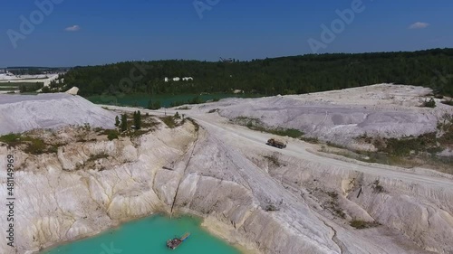 Loaded truck moving along the road at present day kaolin mine. White hilly ground, blue water and clear sky. Green trees at the backdrop. photo