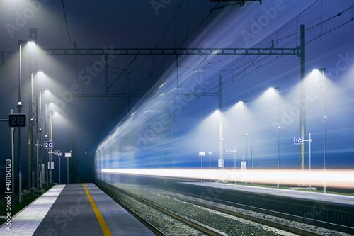 Railway at night. Light trail of passenger train at illuminated railroad station.