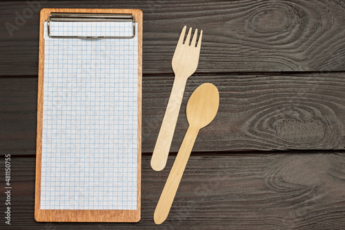 Menu clipboard, wooden fork and spoon on wooden background.