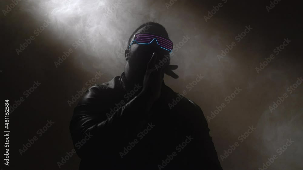90s nightlife. Rap music. Hip hop show. Silhouette of confident brutal man artist in futuristic stylish neon glowing sunglasses performing song on event.