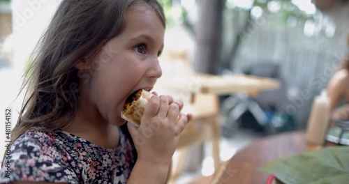 Cute little girl at wooden table eating burrito with blurry background