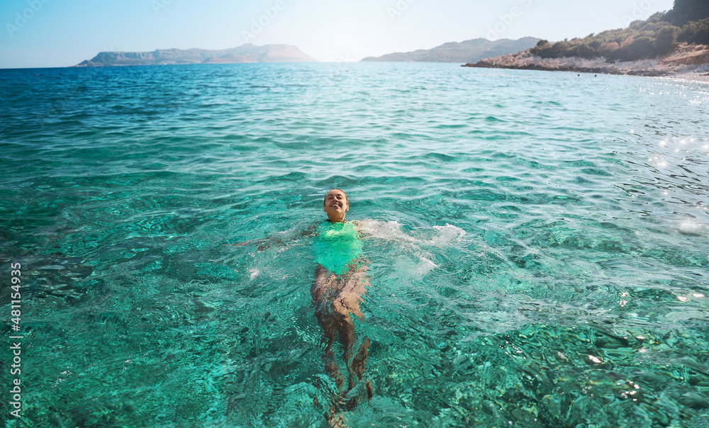Smiling woman lying on her back floating in the sea water, relaxing on ...