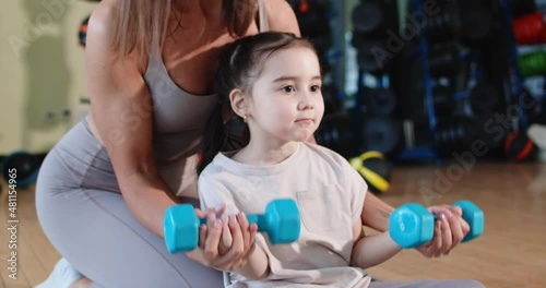 Attractive young mother helping her young daughter do biceps exercises with dumbbells. High Quality. Slow motion.