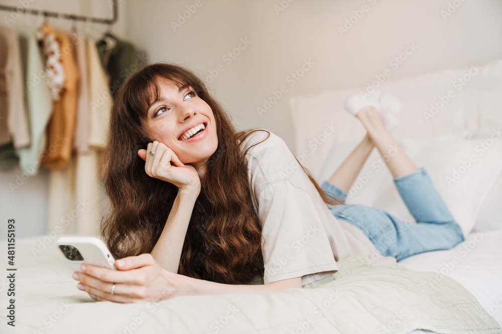White woman smiling and using mobile phone while lying on bed White woman smiling and using mobile phone while lying on bed