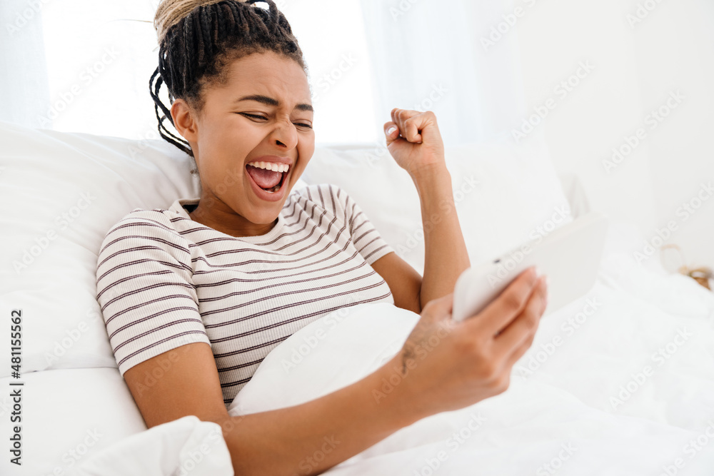 Young black woman playing online game on cellphone while lying on bed Young black woman playing online game on cellphone while lying on bed