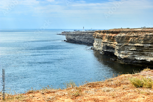 Yellow, white rocky seashore, Chalky cliff. Blue deep calm sea. Cloudy sky. The white lighthouse. The western part of the Crimea, Cape Tarkhankut. Stone pattern. Beautiful natural landscape.