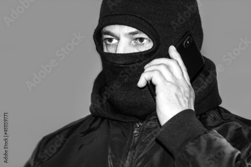 Black and white photo criminal in a black balaclava and a hoodie in the dark. The concept of crime growth, robbery and fraud, unemployment and malice.