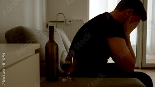 DEPRESSION: Mental suffering of a young man on a sofa in a dim room at home. Alcohol nearby