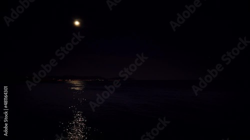 Full moon at night on black sky over sea, coastal region. Moonlight reflecting in water.