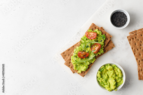 Tasty avocado toasts with  tomatoes cherry and black sesame seeds on white board. Top view. Copy space photo