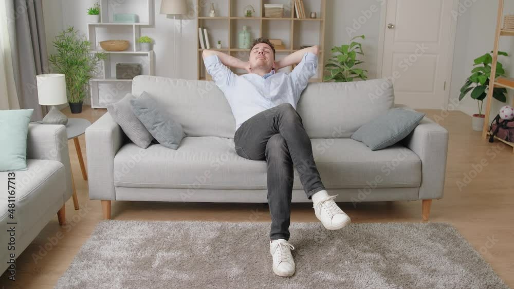 Young relaxed millennial man sit on sofa put hands behind head enjoy fresh air conditioned room spend carefree holidays at modern apartment. Stress free, contemplation, weekend leisure at home concept Young relaxed millennial man sit on sofa put hands behind head enjoy fresh air conditioned room spend carefree holidays at modern apartment. Stress free, contemplation, weekend leisure at home concept