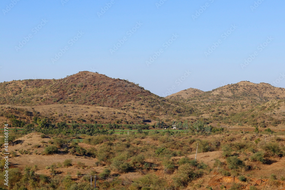 This image was captured near Junagadh Gir Forest in winter time at Gir National Park and Sanctuary Gujarat India. clear sky in mountain, yellow grass and green farmland beautiful countryside landscape