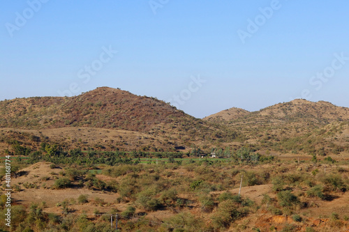 This image was captured near Junagadh Gir Forest in winter time at Gir National Park and Sanctuary Gujarat India. clear sky in mountain, yellow grass and green farmland beautiful countryside landscape