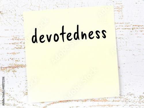Yellow sheet of paper with word devotedness. Reminder concept
