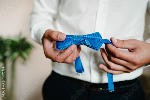 Man straightens his bow tie on shirt at home or dressing bow tie on shirt at room. clothing concept. The groom in wedding morning.